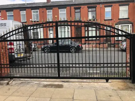 Arched black metal driveway gates with gold spear tops across a terraced street