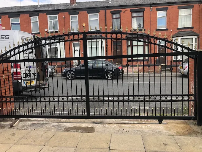 Arched black metal driveway gates with gold spear tops across a terraced street