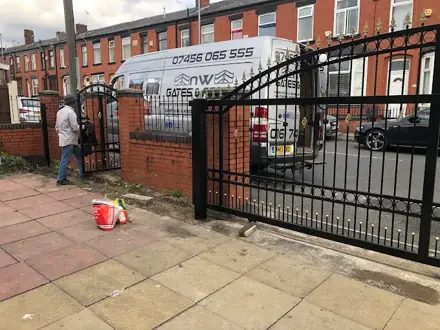 Matching black metal driveway and pedestrian gates with gold details on a brick wall