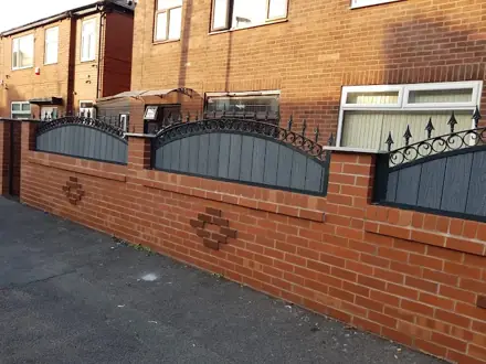 Grey infill panels with decorative black railings fitted above a red-brick wall