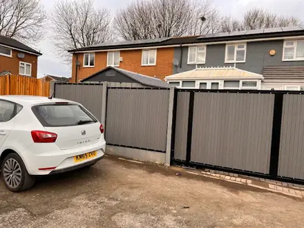 Matching grey composite gates and boundary fencing beside a parked white car