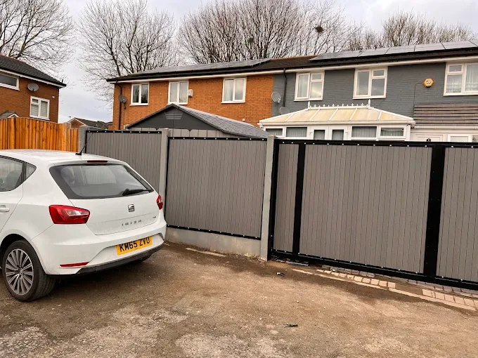 Matching grey composite gates and boundary fencing beside a parked white car