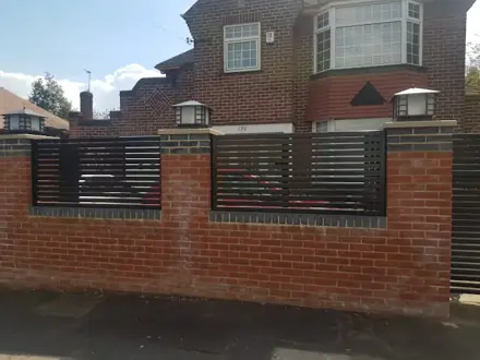 Dark horizontal metal railings fitted between brick pillars on a front wall