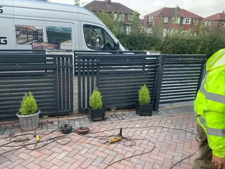 Grey slatted gates and panels on a block-paved drive, with the company van behind
